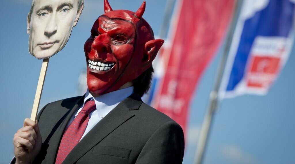 An activist wears a devil's mask which he covers with a picture of Vladimir Putin as part of a protest against the Russian President outside the congress center of the Hanover trade fair on April 7, 2013 in Hanover, western Germany. Photo by AFP
