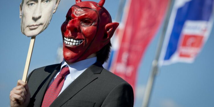 An activist wears a devil's mask which he covers with a picture of Vladimir Putin as part of a protest against the Russian President outside the congress center of the Hanover trade fair on April 7, 2013 in Hanover, western Germany. Photo by AFP
