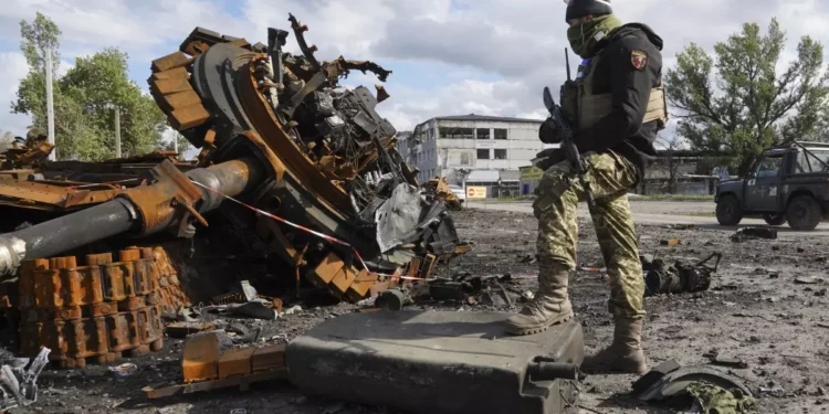 A Ukrainian soldier stands near pieces of a Russian tank Tuesday in the Kharkiv region. (Andrii Marienko / Associated Press)
