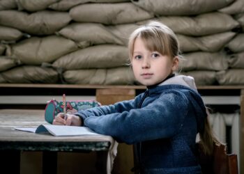 UNICEF/UN0150817/Gilbertson V A child sits in a classroom in Ukraine with sandbags reinforcing the window to protect against shrapnel and bullets.