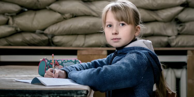 UNICEF/UN0150817/Gilbertson V A child sits in a classroom in Ukraine with sandbags reinforcing the window to protect against shrapnel and bullets.
